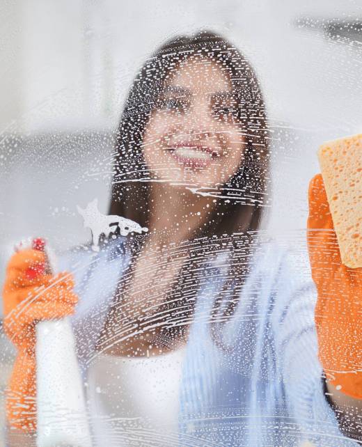 Young woman washing window in rubber gloves with special detergent. Concept of cleaning glass or window at home.